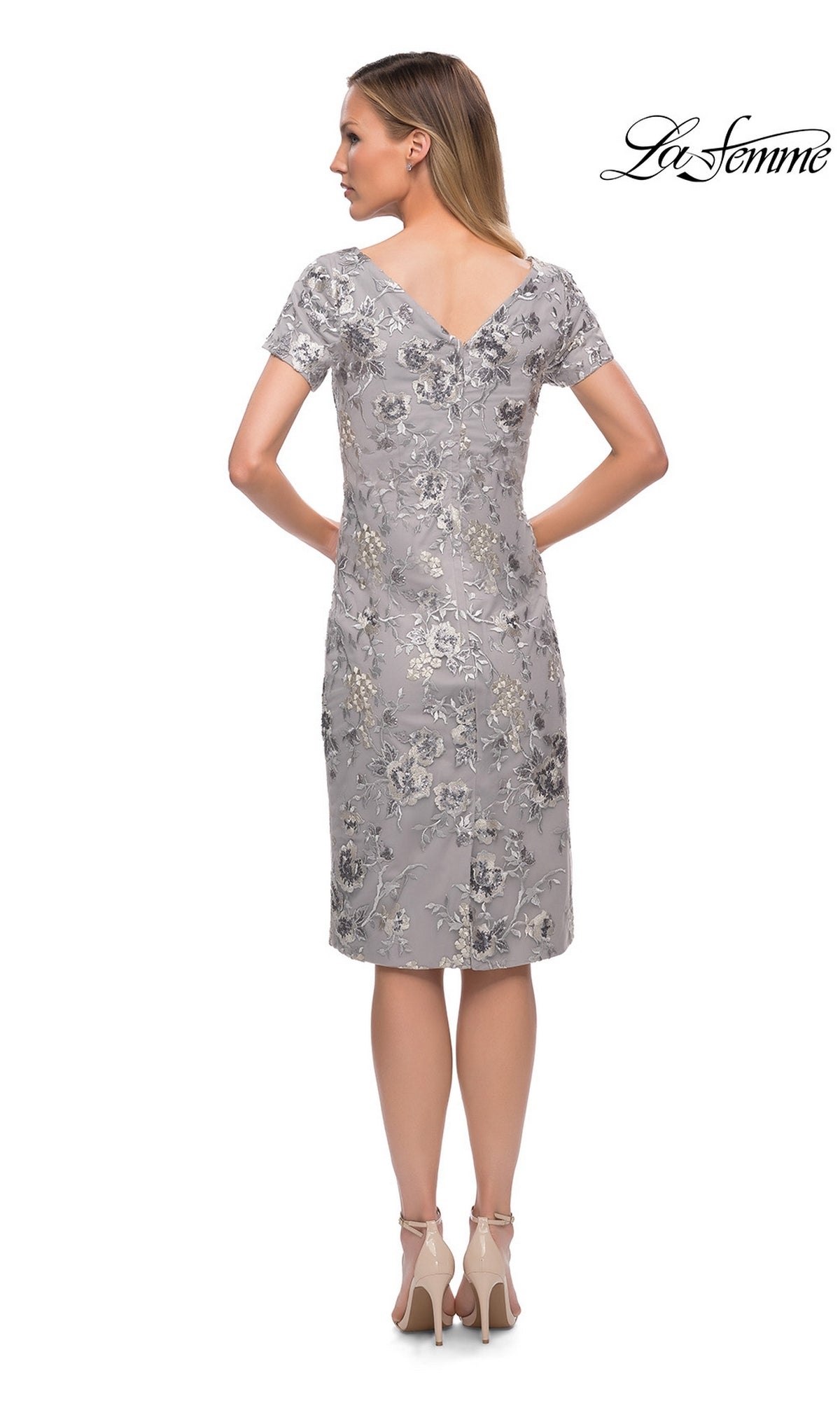 Woman with her back to the camera in a modest silver floral-lace Knee Length Wedding Guest Dress: La Femme 29824 and beige heels. โLa Femmeโ logo in upper right corner.